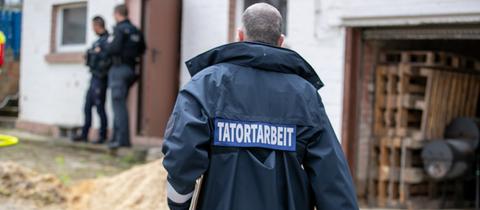 Das Bild zeigt einen Polizisten von hinten. Er trägt kurze graue Haare und eine blaue Jacke, auf der das Wort "Tatortarbeit" steht.