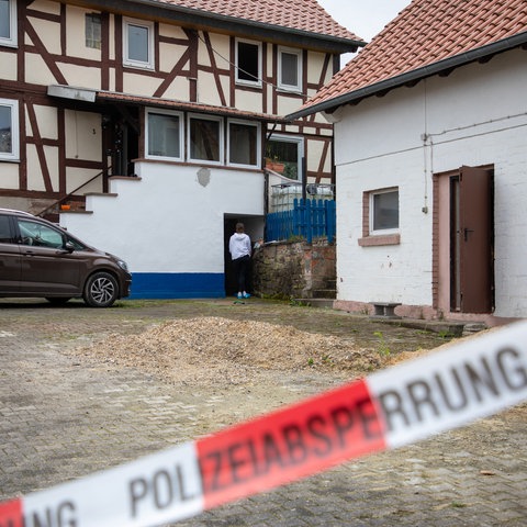 Das Bild zeigt einen SEK-Einsatz auf einem Hof mit Fachwerkhaus. Im Vordergrund ist ein rot-weißes Polizeiabsperrband zu sehen.