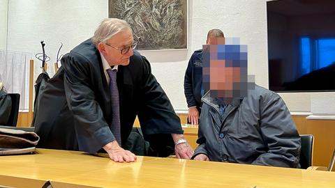 Der angeklagte Busfahrer sitzt rechts neben seinem Anwalt an einem Tisch im Landgericht Fulda. Im Hintergrund steht ein Polizist.