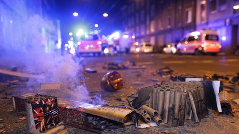 Abgebrannte Böller liegen nach der Silvesternacht auf einer Straße, während im Hintergrund Einsatzkräfte der Feuerwehr stehen.