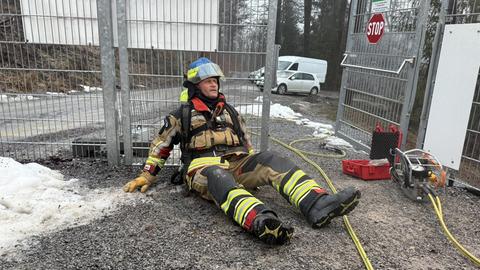 Ein Feuerwehrmann liegt in voller Montur auf dem Rücken und stützt sich mit den Händen ab. Er trägt einen Helm und schwere Stiefel.