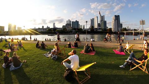 Menschen sitzen auf Klappstühlen auf den Mainwiesen, im Hintegrund Skyline