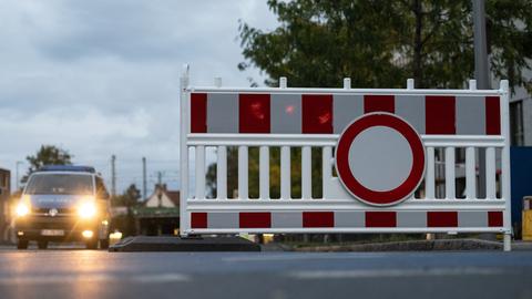 Ein Absperrschild mit einem Polizeiwagen im Hintergrund.