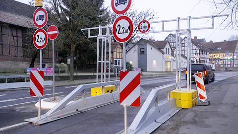 Foto: Blick auf Gestell auf einer Straße, das die Form einer überdimensionalen Tür hat und rechts und links von Schildern mit den Zeichen "Lkw" und "2,2m" begleitet wird.