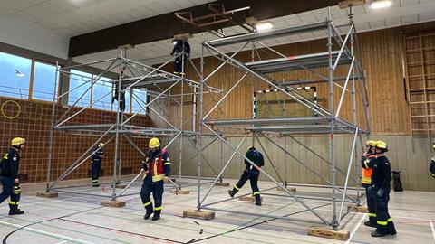 Einsatzkräfte stehen rund um ein Gerüst, das in einer Sporthalle aufgebaut ist.