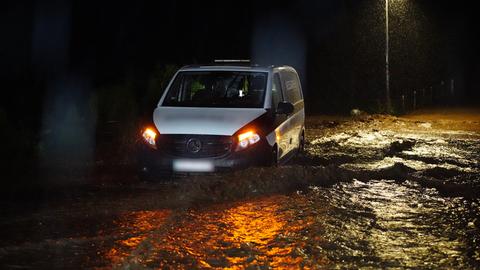 Ein Auto versinkt zur Hälfte auf einer überfluteten Straße im Wasser.