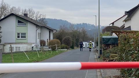 Feuerwehrleute laufen hinter einer Absperrung zu einem Wohnhaus. 