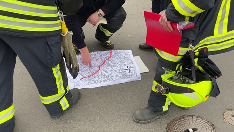 Feuerwehrleute laufen hinter einer Absperrung zu einem Wohnhaus. 