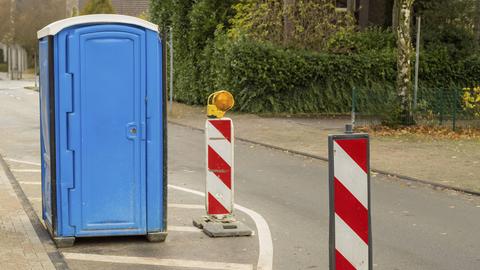 Blaue tragbare Toilette steht auf einer Straße neben Verkehrswarnmasten, die auf Baustellen hinweisen