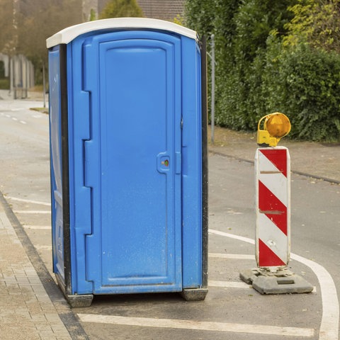 Blaue tragbare Toilette steht auf einer Straße neben Verkehrswarnmasten, die auf Baustellen hinweisen