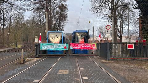 Straßenbahnen stehen vor einem verschlossenen Tor, über den Fenstern hängen Streikplakate