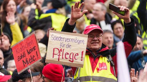 Teilnehmer der Schlusskundgebung zu der die Gewerkschaft Erziehung und Wissenschaft (GEW Hessen) aufgerufen hat, halten ein Plakat mit der Aufschrift „Sondervermögen für die Pflege!“ und "Klatschen zahlt keine Miete!". 