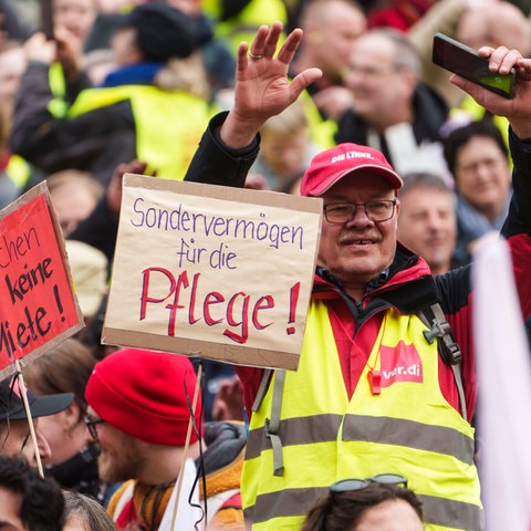 Teilnehmer der Schlusskundgebung zu der die Gewerkschaft Erziehung und Wissenschaft (GEW Hessen) aufgerufen hat, halten ein Plakat mit der Aufschrift „Sondervermögen für die Pflege!“ und "Klatschen zahlt keine Miete!". 