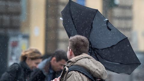 Passanten, einer davon hält einen umgestülpten Regenschirm fest.