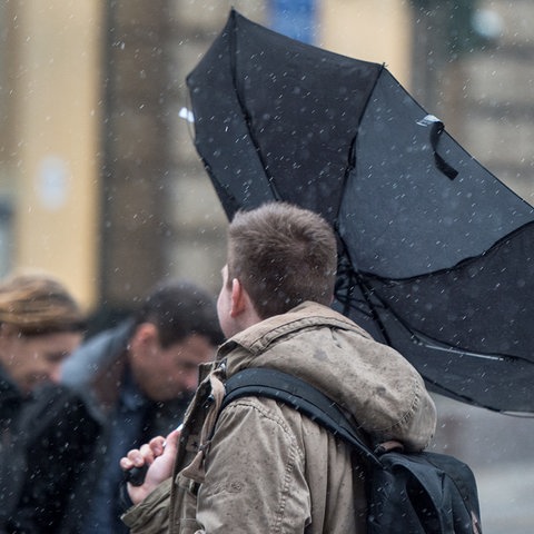 Passanten, einer davon hält einen umgestülpten Regenschirm fest.