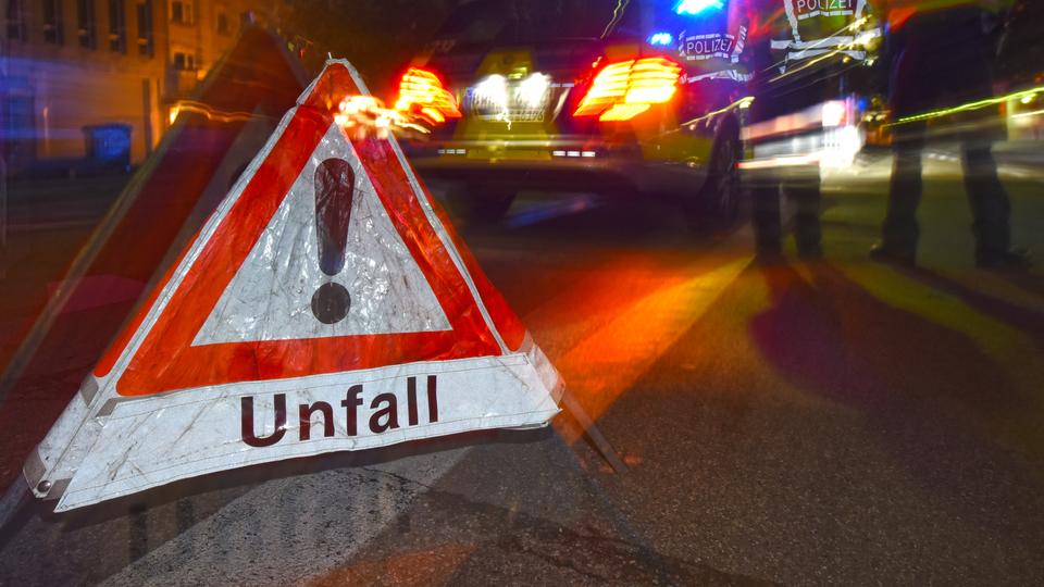 Warndreieck mit Aufschrift Unfall - im Hintergrund ein Polizeiauto (Nachtaufnahme)