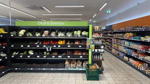 Blick in einen Supermarkt: im Vordergrund frisches Obst und Gemüse. In einem Korb auf dem Boden sind Kartofffeln.