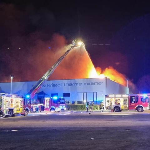 Brennendes Gebäude, davor Feuerwehrfahrzeuge