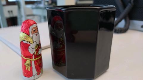 Schwarze Kaffeetasse mit Ecken, kleiner Schoko-Nikolaus mit rotem Gewand daneben