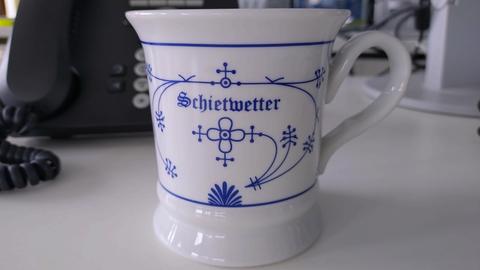 Weiße Tasse mit feinen blauen Schnörkeln und der Aufschrift "Schietwetter"