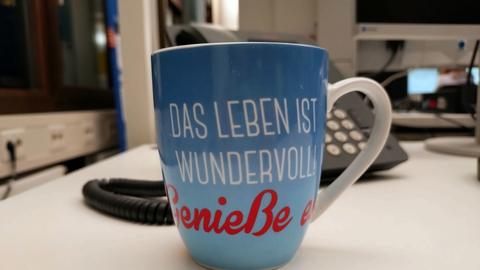 Eine blaugrundige Kaffeetasse auf der steht "Das Leben ist wundervoll! Genieße es!"