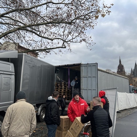 Ein Container steht an einer Straße am Frankfurter Mainufer, Männer laden Paletten mit zurückgegebenen Weihnachtsmarkt-Tassen auf.