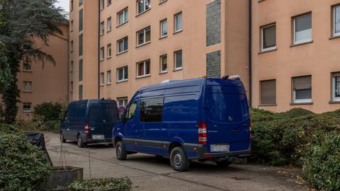 Vor einem Mehrfamilienhaus mit terrakottafarbener Fassade stehen zwei dunkelblaue Transporter. 