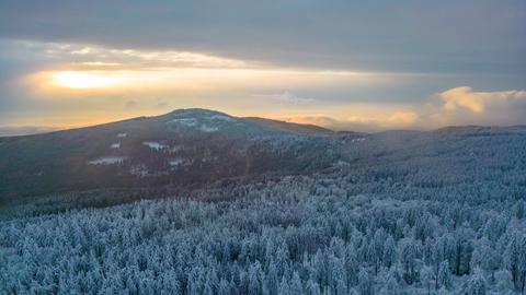 Schneebedeckte Bäume und Sonnenlicht, das durch die Wolkendecke bricht, auf und über den Bergen des Taunus