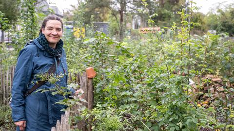 Sträucher und Büsche stehen auf einer abgezäunten Fläche, daneben steht Julia Auer, die in die Kamera guckt. 