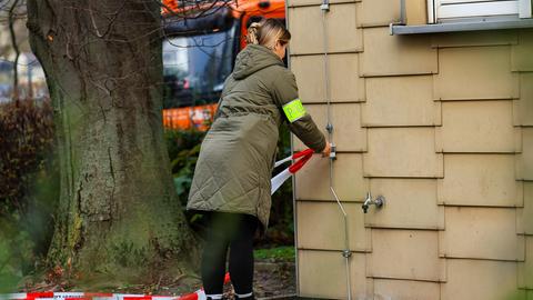 Polizei am Tatort in Bensheim: Eine Frau mit Armbinde mit Aufdruck "Polizei" befestigt an einer Hauswand ein rot-weiß-gestreiftes Absperrrband