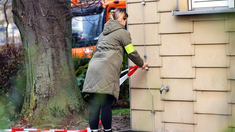 Polizei am Tatort in Bensheim: Eine Frau mit Armbinde mit Aufdruck "Polizei" befestigt an einer Hauswand ein rot-weiß-gestreiftes Absperrrband