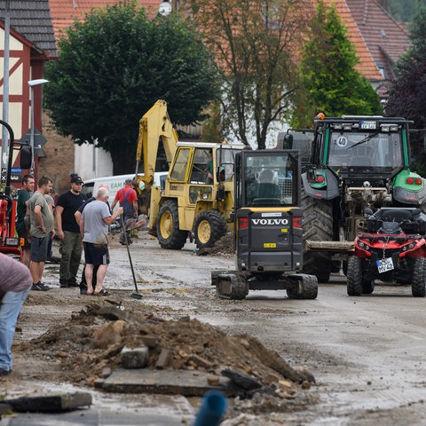 Straßen sind stark beschädigt, Menschen räumen Schutt mithilfe von Baggern weg.