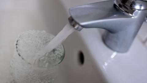 Tinkwasser läuft aus dem Wasserhahn im Badezimmer in ein Glas.