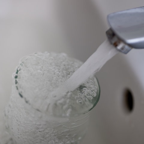 Tinkwasser läuft aus dem Wasserhahn im Badezimmer in ein Glas.