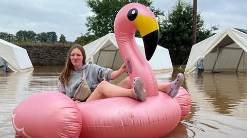 Frau sitzt auf einem aufblasbaren Flamingo während Überschwemmungen