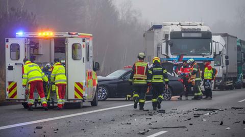 Einsatzkräfte von Feuerwehr und Rettungsdienst auf der Autobahn, schwarzer Pkw schwer beschädigt, Trümmerteile auf der Fahrbahn