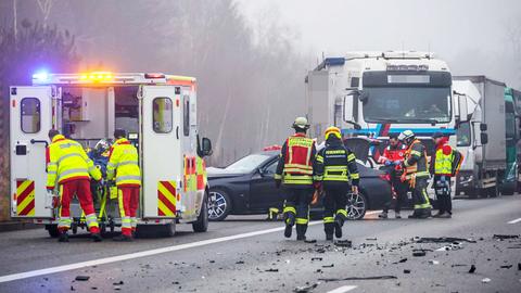 Einsatzkräfte von Feuerwehr und Rettungsdienst auf der Autobahn, schwarzer Pkw schwer beschädigt, Trümmerteile auf der Fahrbahn