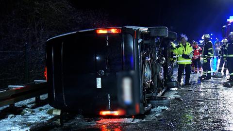 Ein schwarzer Sprinter liegt seitlich auf der glatten Fahrbahn, daneben stehen Einsatzkräfte von Polizei und Feuerwehr.