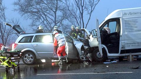 Feuerwehrleute und ein Sanitäter beugen sich über und in einen silbernen Unfall-Pkw, dessen Heckklappe und Türen geöffnet sind; rechts davon der zerstörte Transporter, auf den der Pkw gekracht ist