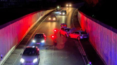 Zwei frontal zusammengestoßene Kleinwagen stehen in einer Unterführung, Polizei leitet Verkehr daran vorbei; Dunkelheit