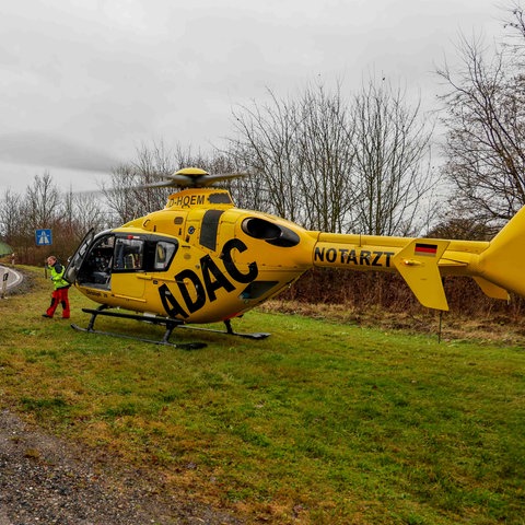 Ein Rettungshubschrauber steht auf einer Wiese neben einer Autobahnauffahrt.