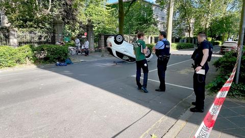 In einer Straße liegt ein Cabrio liegt nach einem Überschlag auf seinem Dach. Polizeikräfte stehen daneben.