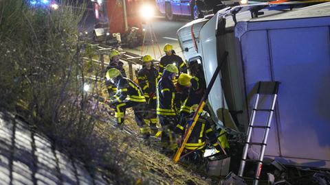 Mehrere Rettungskräfte am Fahrerhaus eines zerstörten Lasters, der am Fahrbahnrand einer Autobahn liegt.