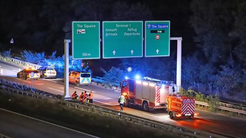 Feuerwehr- und Polizeiwagen auf der Autobahn in der Nacht. Auf einem Schild steht unter anderem "Terminal 1", "Ankunft" und "Abflug".