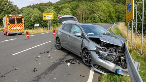 Beschädigtes Auto an Leitplanke, im Hintergrund ein Rettungswagen