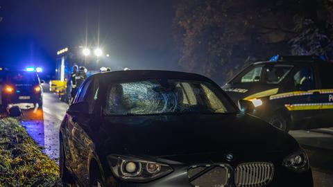 Ein Auto mit zerspöitterter Scheibe, im Hintergrund Polizeiwagen und Rettungskräfte