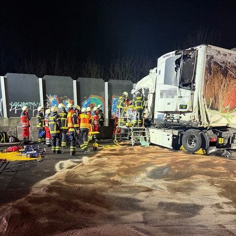 Front eines zerstörten Lastwagens, davor viele Einsatzkräfte, im Vordergrund eine mit Sand abgestreute Ölspur