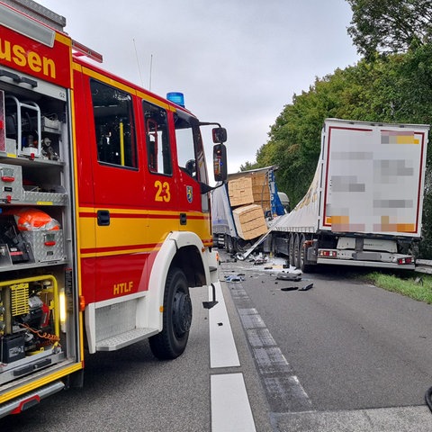 Feuerwehrwagen auf der Autobahn, daneben zwei ineinander gefahrene Lastwagen, einer hat Ladung verloren