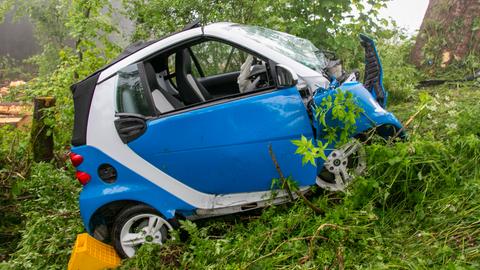 Ein bei einem Unfall beschädigtes Auto steht im Gebüsch neben einer Straße.
