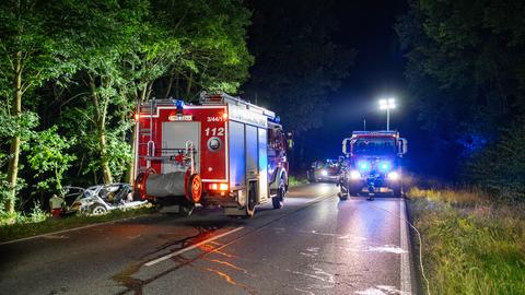 Das Wrack eines Autos liegt nach einem Unfall neben einer Landstraße, daneben Einsatzfahrzeuge.